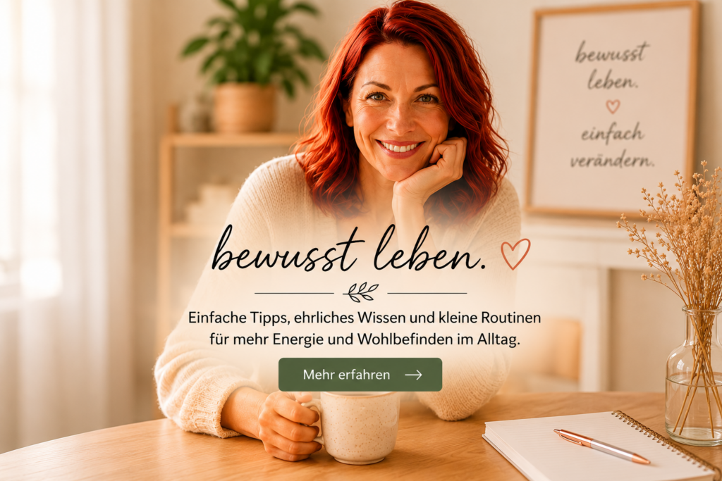 Rothaarige Frau sitzt lächelnd mit einer Tasse am Tisch – Startbild zum Thema bewusst leben, mehr Energie und Wohlbefinden im Alltag.